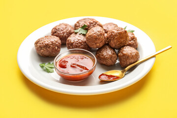 Plate with tasty meat balls, parsley, sauce and spoon on yellow background