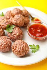 Plate with tasty meat balls, parsley, sauce and spoon on yellow background, closeup