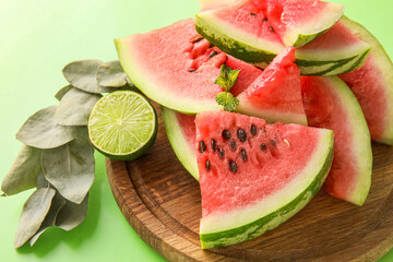 Cutting board with slices of watermelon, lime and eucalyptus branch on green background
