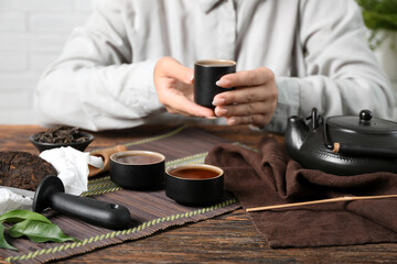 Woman with cup of puer tea at wooden table, closeup