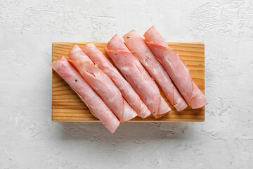 Wooden board with rolled slices of tasty ham on light background