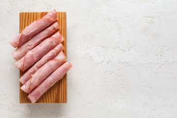Wooden board with rolled slices of tasty ham on light background