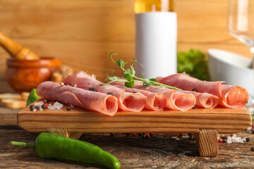 Board with rolled slices of tasty ham on wooden table