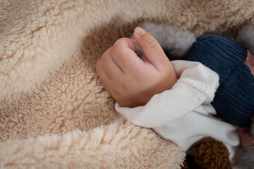 close-up of small hands of a 3-month-old Asian newborn with her left hand attached to the body of a little girl lying on a soft bed in the bedroom looking relaxed.