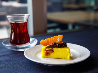 Delicious banana mango orange mousse cake slice with chocolate cream and caramelized orange on top on black table background. Restaurant menu and confectionery concept. Close-up. Copy space.