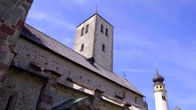 Wide tracking shot revealing the exterior and bell tower of the romanesque Collegiate church of San Candido, Italy.