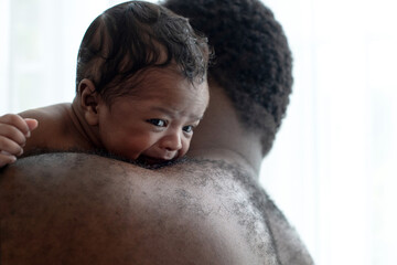 Obraz premium Shirtless African father cuddling baby son resting over shoulder, father holds and comforts the baby, closeup and selective focus