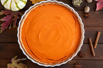 Traditional pumpkin pie with whipped cream and cinnamon on dark wooden background. Homemade pastry for Thanksgiving or Halloween. Copy space.