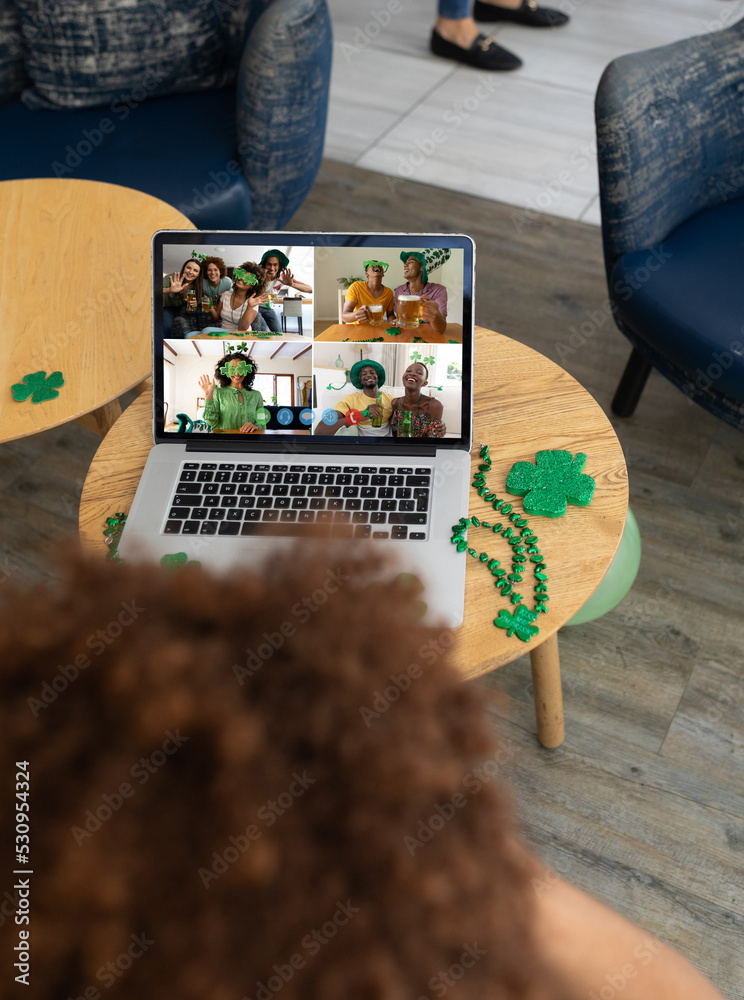 Poster Mixed race man celebrating st patrick's day making video call to friends on laptop at a bar