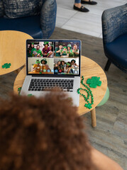 Mixed race man celebrating st patrick's day making video call to friends on laptop at a bar