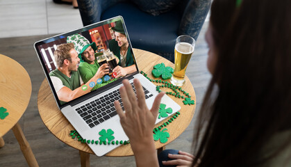 Caucasian woman with beer making st patrick's day video call waving to friends on laptop at bar