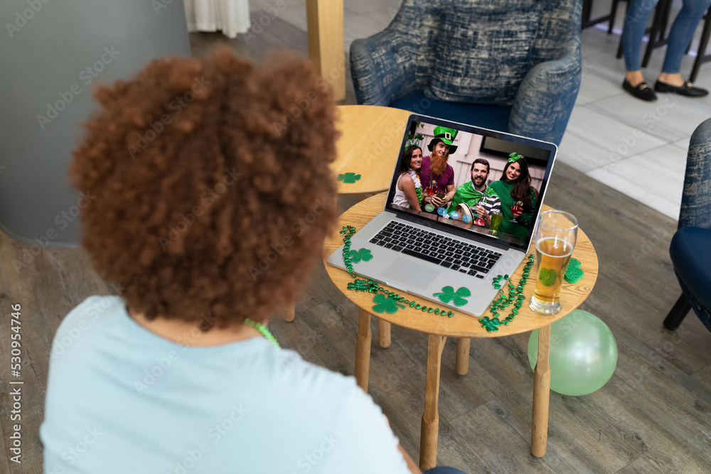 Poster Mixed race man at bar making st patrick's day video call to group of friends on laptop screen