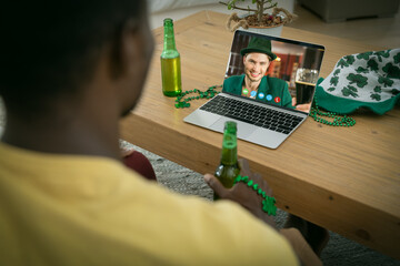 African american man holding a beer having a video call on laptop at home