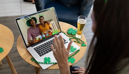 Caucasian woman with beer at bar making st patrick's day video call waving to friends on laptop
