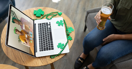 Mixed race woman at bar holding beer making st patrick's day video call to friends on laptop