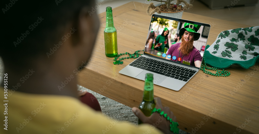 Sticker African american man holding beer making st patrick's day video call to friends on laptop at home