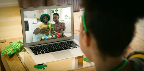 Mixed race woman making st patrick's day video call to happy couple holding beers on laptop at home