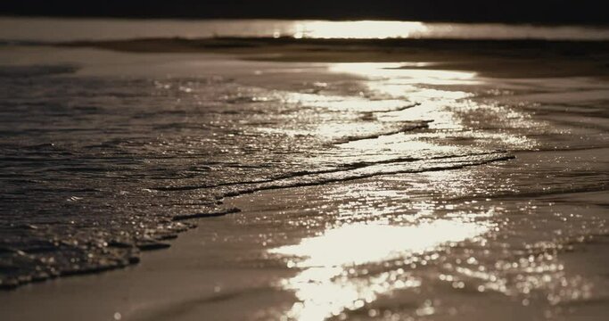 夕日に照らされてキラキラ輝く　リゾートの砂浜の海の波のローアングル　スローモーション　バカンス・観光・旅行・夏休みのイメージ