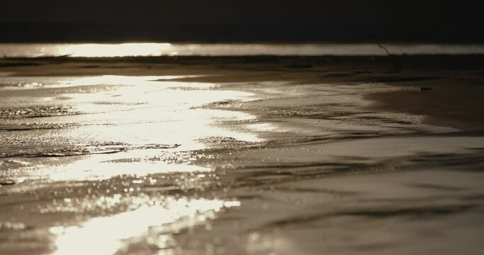 夕日に照らされてキラキラ輝く　リゾートの砂浜の海の波のローアングル　スローモーション　バカンス・観光・旅行・夏休みのイメージ	
