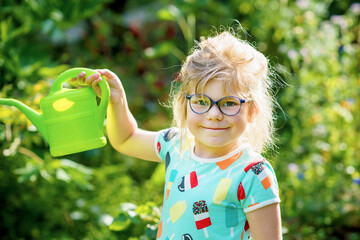 Little girl in a garden with green watering pot. Preschool child using rainwater to water flowers...
