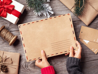 The child holds in his hands an envelope with a letter to Santa Claus on the background of Christmas decorations, a template for the designer