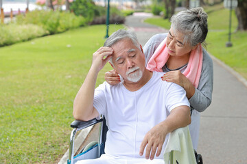 Asian senior woman or caregiver helping and consoling senior man walk with wheelchair at park outdoor. Elderly wife taking good help care and support of elder husband patient outside the house.