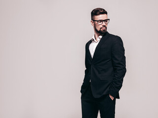 Obraz na płótnie Canvas Portrait of handsome confident stylish hipster lambersexual model. Sexy modern man dressed in elegant black suit. Fashion male posing in studio near white wall. Isolated on grey. In spectacles