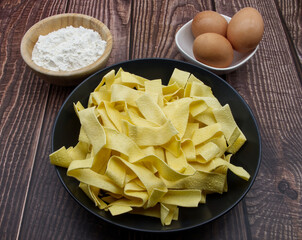 Traditional uncooked Italian Pappardelle on wooden table.
