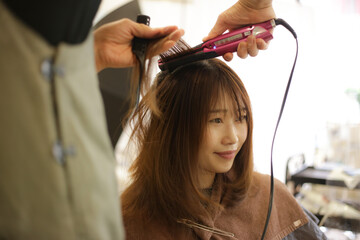 Fototapeta premium 女性の髪にヘアアイロンをかける男性美容師