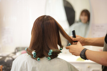 女性の髪にパーマロッドを巻く男性美容師
