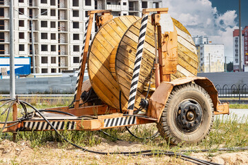 Obraz premium Wooden reel with high voltage cable mounted on a trailer for easy transport and stowage. Laying a high-voltage power cable in the ground. Laying of cables, laying of underground communications.