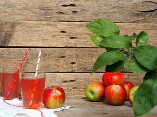 Glass of apple juice and red apple on wooden background.