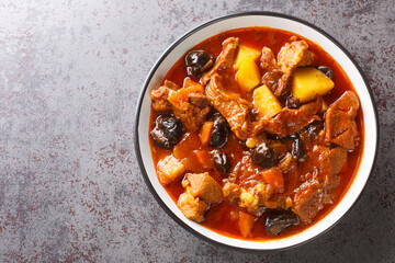 Khoresht Aloo Stewed lamb meat with dried plums or prunes, tomato, onion, potato, carrot and garlic closeup in the bowl on the table. Horizontal top view from above