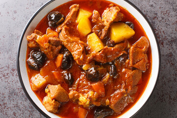 Plum stew with lamb, prunes, tomatoes, carrots, onions, potatoes and spices close-up on a plate on the table. horizontal top view from above