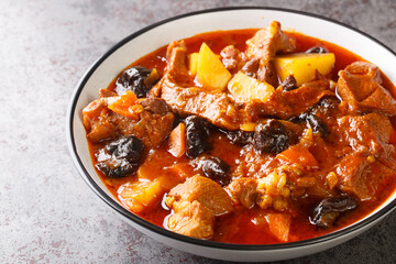 Plum stew with lamb, prunes, tomatoes, carrots, onions, potatoes and spices close-up on a plate on the table. horizontal