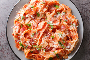Italian pasta food homemade pappardelle with with bacon and tomato, parmesan cheese and chopped parsley closeup in the plate on the table. Horizontal top view from above