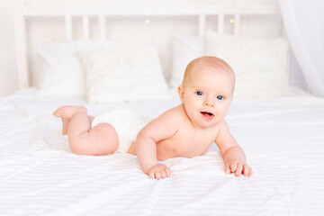 cute baby girl in a crib on a white cotton bed lying on her stomach in the nursery smiling, newborn morning