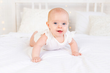 baby girl smiles lying on her stomach on a white cotton bed at home