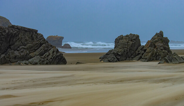 large rock formations on the beach with waves crashing in the background