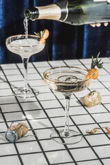 Two glasses of champagne against the background of tiles and blue curtains and a bottle of champagne.