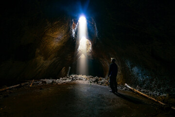 Adventurous athletic male standing in a lava tube looking at the sunlight shinning down into the cave through holes in the ceiling.