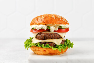 Homemade grilled burger on a sesame seed bun with tomatoes, sauce, cutlets ant lettuce.
