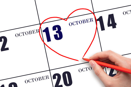 A woman's hand drawing a red heart shape on the calendar date of 13 October. Heart as a symbol of love.