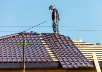 Workers install metal roofing on the wooden roof of a house.