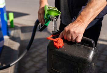 A man fills fuel in a plastic can at a gas station