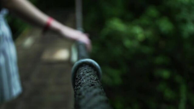 Lady's hand holding on to a rope of a hanging rope bridge as she crosses