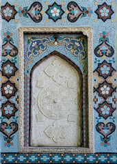 Closeup of beautiful traditional geometric and floral design in white stucco with blue mosaic frame on the exterior wall of ancient Sar-i-Mazor mausoleum, Istaravshan, Sughd region, Tajikistan