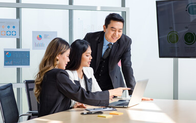 Millennial Asian cheerful successful professional male businessman mentor advising sharing ideas with female businesswomen colleagues in formal suit working with laptop computer together in office