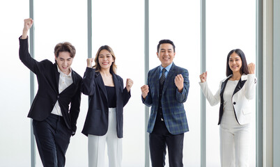 Millennial Asian successful professional male businessmen and female businesswomen in formal suit standing side by side smiling hodling fists up celebrating achievement together in company office