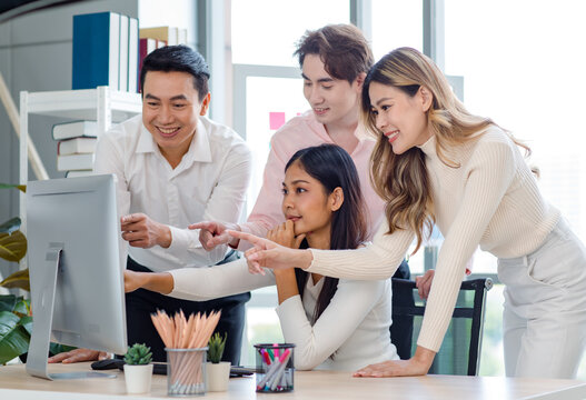 Millennial Asian beautiful successful professional businesswoman sitting smiling pointing finger showing data information on computer monitor to male businessmen female colleague in company office